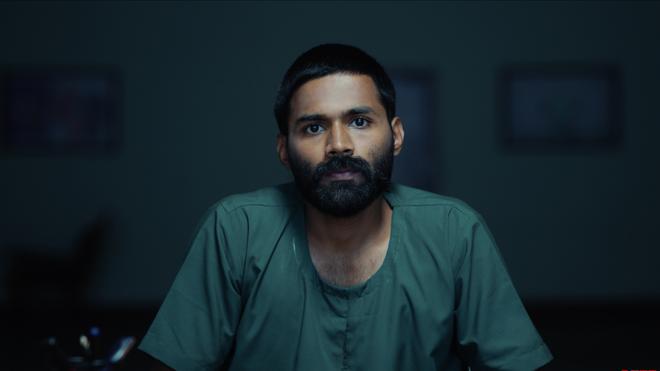 “Stephen move review seated in a police interrogation room with investigators Michael and Seema questioning him in the Tamil movie Stephen.”